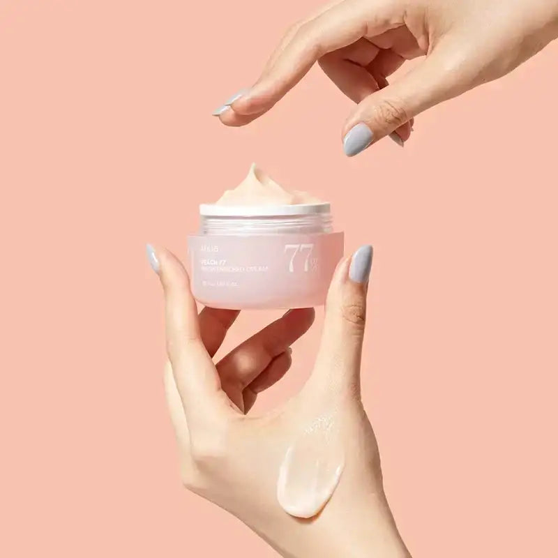 Un pot translucide rose pâle de crème hydratante à 77%, avec un couvercle blanc et une étiquette minimaliste.